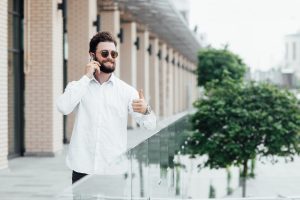 A man on an outdoor activity of his office. wears sunglasses during on-call in the front of buildibg